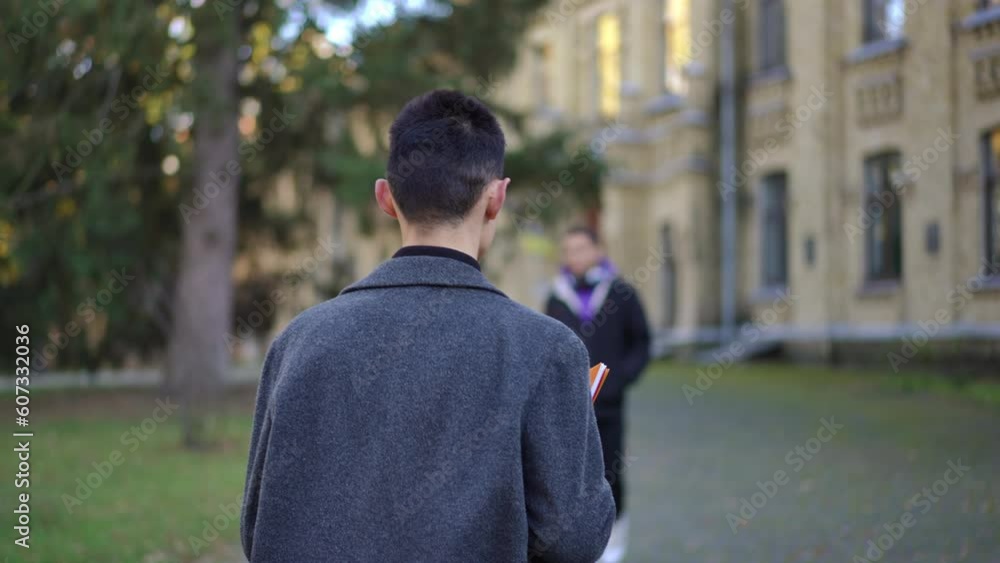 Back view young Caucasian man strolling in slow motion at college campus with African American student passing leaving. Tracking shot of confident intelligent guy walking to university Back view young Caucasian man strolling in slow motion at college campus with African American student passing leaving. Tracking shot of confident intelligent guy walking to university