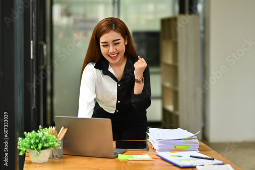 Surprised businesswoman looking at laptop screen, making winner yes gesture, celebrating business success