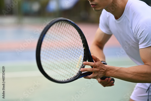 Male tennis player focused in ready position to receive a serve, practicing for competition on a court © Prathankarnpap