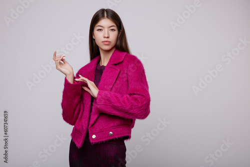 Fashion photo of a beautiful elegant young asian woman in a pretty pink fuchsia dress, jacket posing on white, soft gray background. Studio Shot, portrait. Slim figure. 