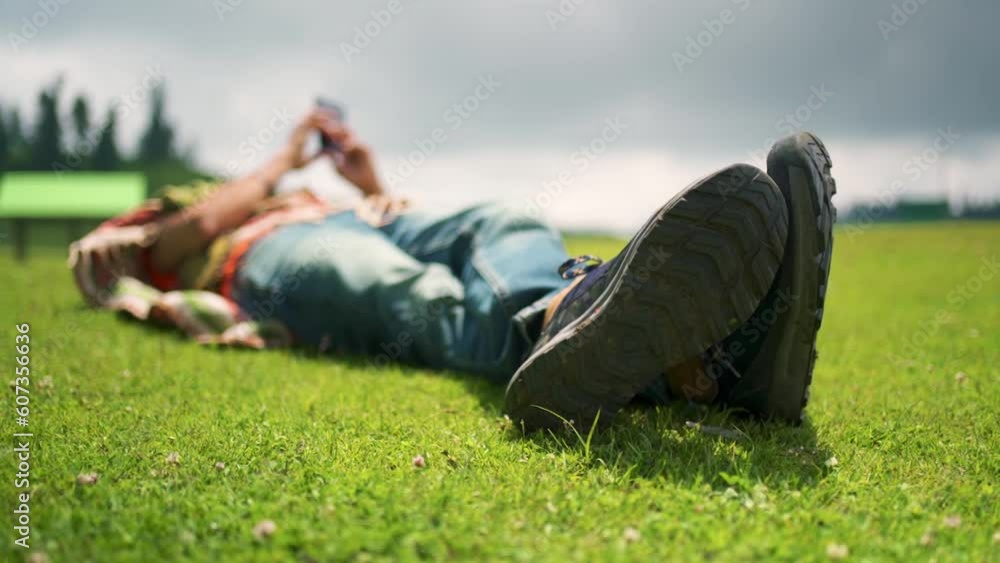 Selective focus of a person lying on green grass in a field under a cloudy sky