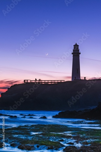 Vertical shot of a lighthouse against a purple sky with half-moon