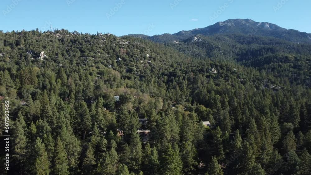 Drone shot over green forested hills and meadows under sunny blue sky Drone shot over green forested hills and meadows under sunny blue sky