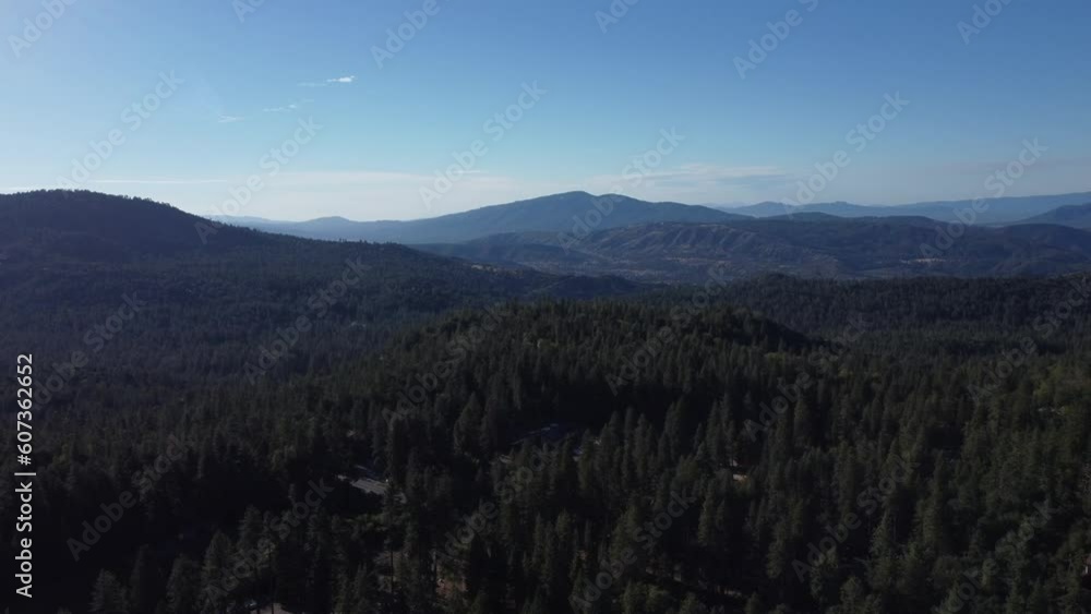 Drone shot over green forested hills and meadows under sunny blue sky Drone shot over green forested hills and meadows under sunny blue sky