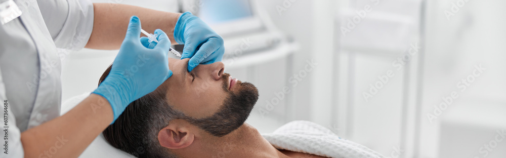 Woman in uniform does filler injection in eyebrow of middle aged client in beauty clinic Woman in uniform does filler injection in eyebrow of middle aged client in beauty clinic
