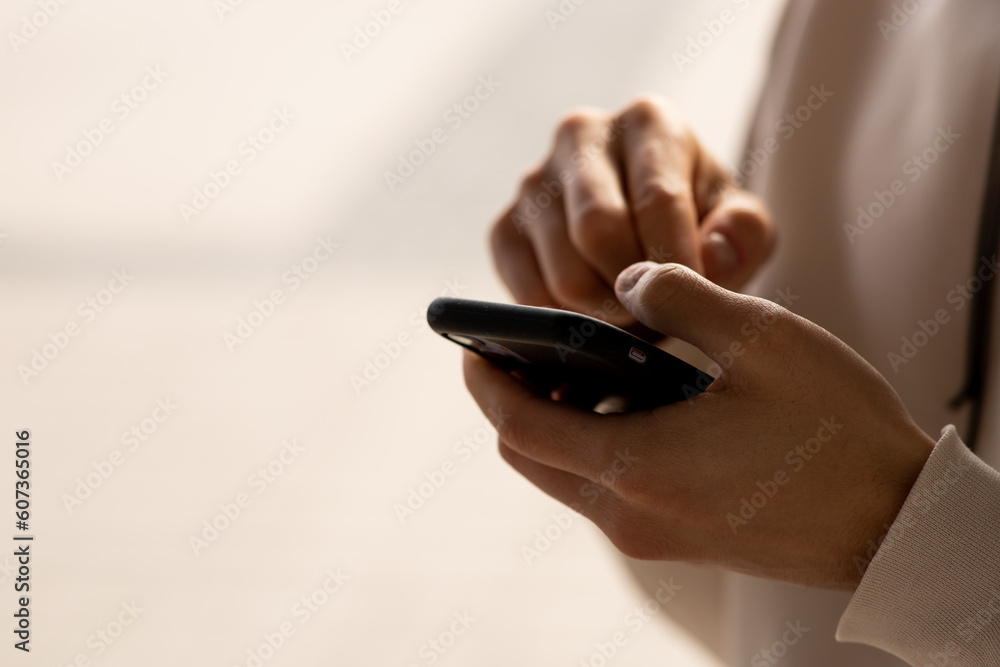 Cropped view of man tapping smartphone screen. A man in a white sweater is writing something on his smartphone. Cropped view of man tapping smartphone screen. A man in a white sweater is writing something on his smartphone.
