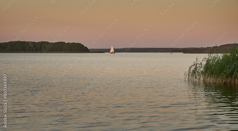 Small boat swimming in the waters of a calm lake surrounded by the dense forest under the sunset sky