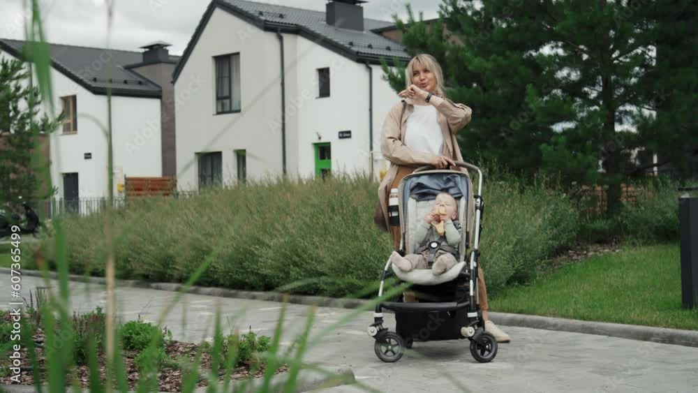 Long shot of young Caucasian woman recording voice message using smart watch during walk with her baby Long shot of young Caucasian woman recording voice message using smart watch during walk with her baby