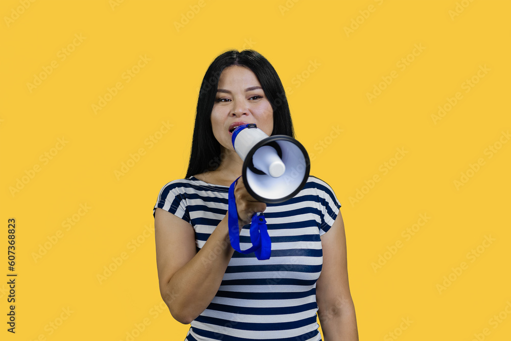 Fototapeta premium Young asian woman saying something in a megaphone. Isolated on yellow.