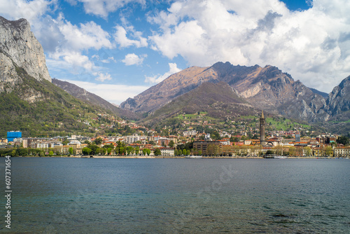 Buildings of the city of Lecco on the shores of Lake Como surrounded by mountains in the background. Sailboats on the waters of the lake and the waterfront. © Piotr