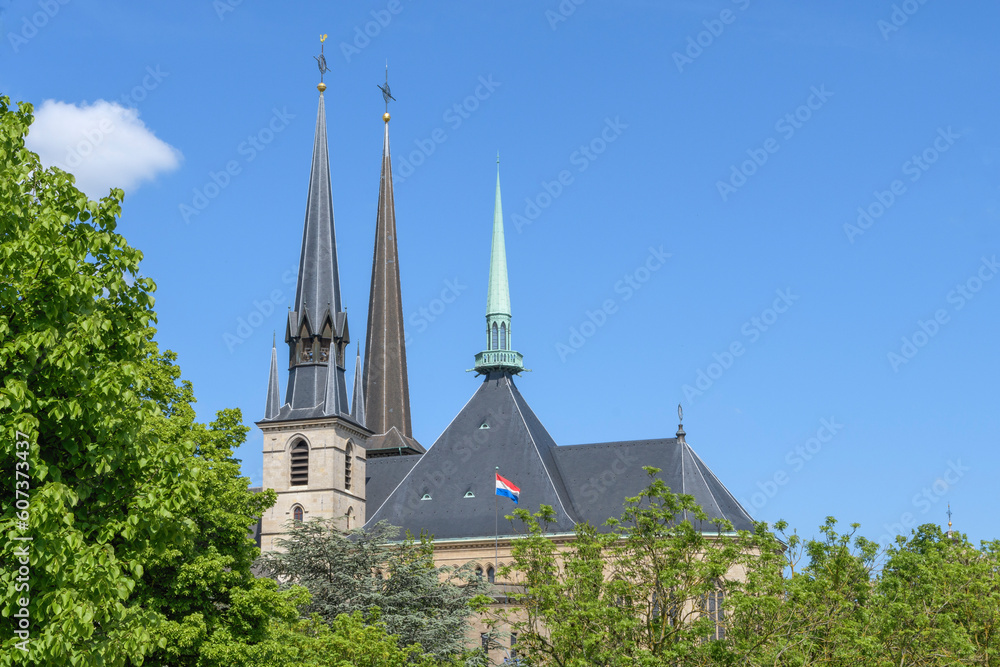 Fragment of the main cathedral of Luxembourg. The spiers of the towers of the central cathedral against the backdrop of a bright spring sky and fresh foliage of trees.