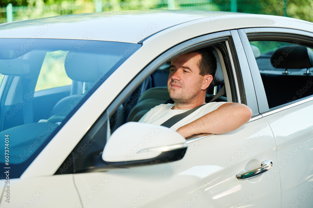 Confident man looking straight while sitting in white car. Adult man looking through window of his car.
