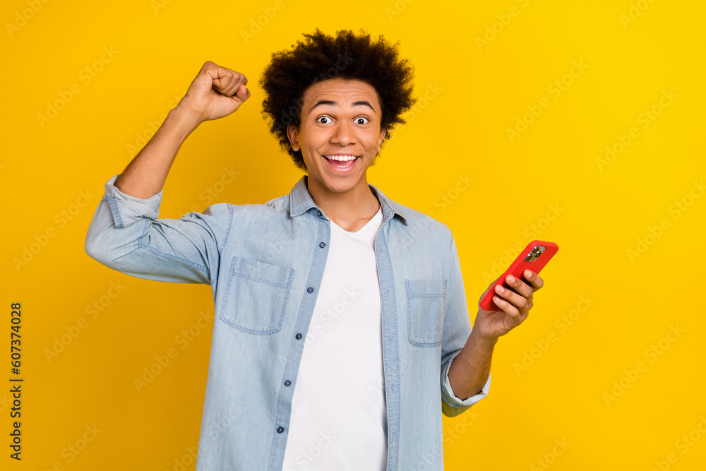 Photo of funky lucky guy dressed denim shirt rising fist texting apple iphone isolated yellow color background Photo of funky lucky guy dressed denim shirt rising fist texting apple iphone isolated yellow color background