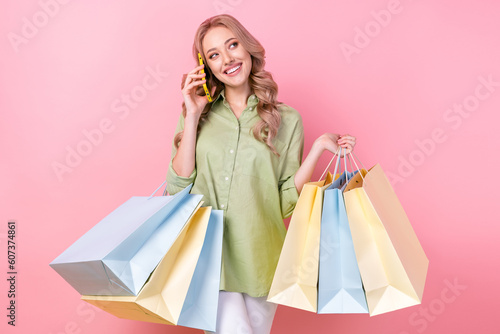Photo of sweet dreamy woman dressed green shirt holding bargains talking gadget looking empty space isolated pink color background