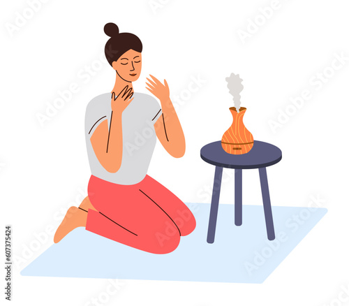 Girl sitting opposite aroma diffuser of essential perfume oil, enjoying smell fragrance.