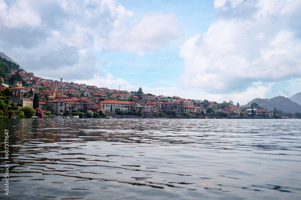 Obraz premium Picturesque town at lake Como. Colourful motley Mediterranean houses at the beach coastline among green trees. Popular health resort and touristic location. Summer day landscape.