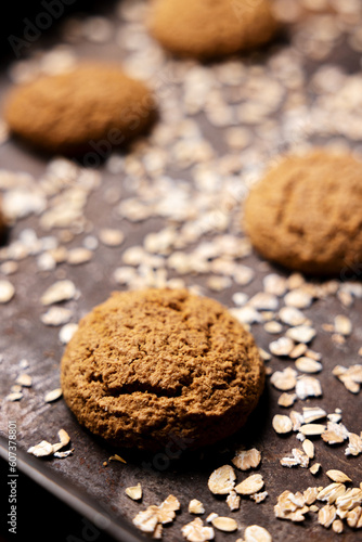 Craft and rustic four oatmeal cookies. Dark food aesthetics, black background with several oat flakes.