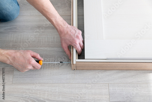 Worker tightens a door frame with a screw. Repair and decoration of apartments. Installation and installation of interior doors. Carpentry work. Working with a screwdriver.