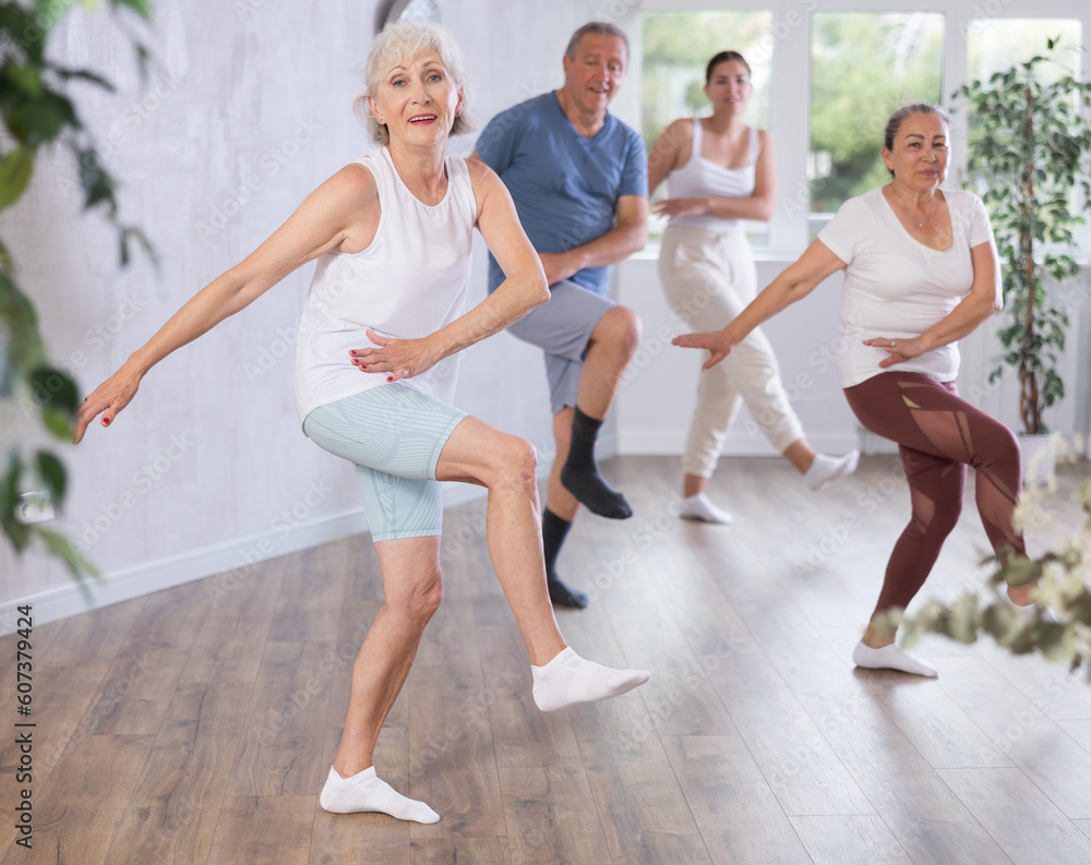 Group session of modern fitness for amateurs in studio. Mature lady with senior class s visitor actively moves and learns to dance hip hop