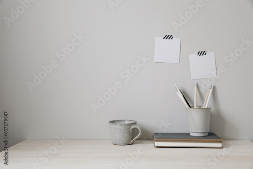 Office table. Empty desk with office supplies and beige wall copy space. Pencils holder, notebooks and cup of coffee. Blank note pad mockups, striped washi tape. Elegant interior, work break concept.