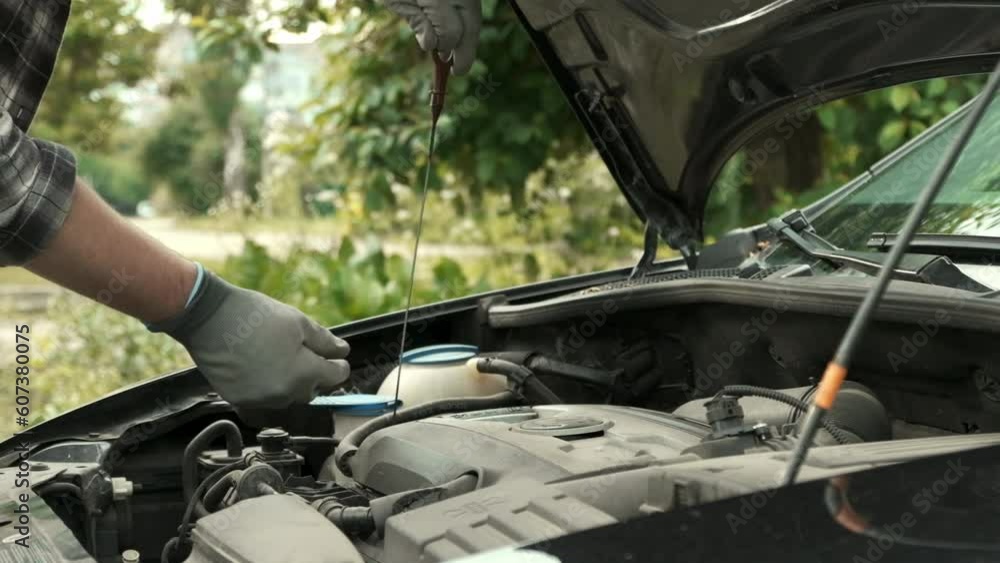 Man using dipstick to check the oil level in a car engine under the hood of the car. Slow motion of engine service performance. Man using dipstick to check the oil level in a car engine under the hood of the car. Slow motion of engine service performance.