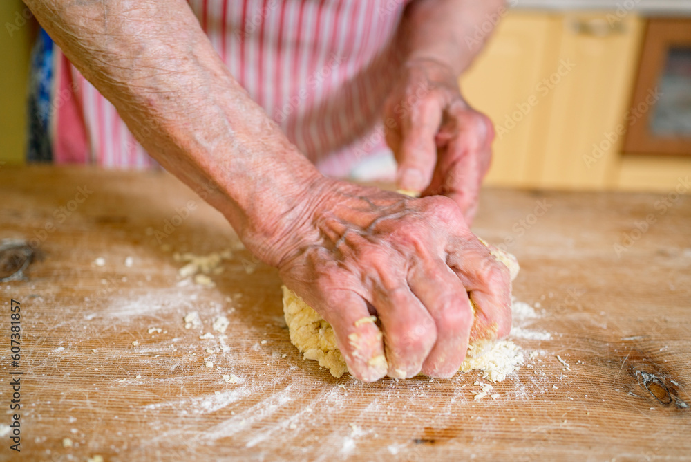grandmother kneads dough, prepares noodles in the kitchen at home. Senior woman hands are rolling out dough in flour with a rolling pin in her home kitchen. 