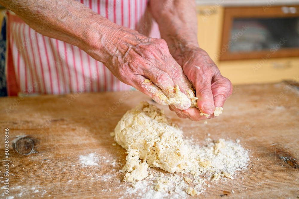 grandmother kneads dough, prepares noodles in the kitchen at home. Senior woman hands are rolling out dough in flour with a rolling pin in her home kitchen. 