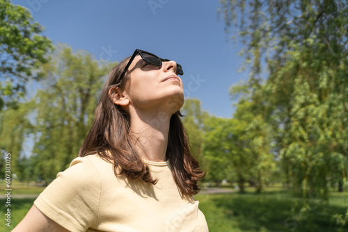 Fitness woman in yellow t-shirt breathing of fresh air. Female relaxing, doing yoga breathing or calm exercise in park.