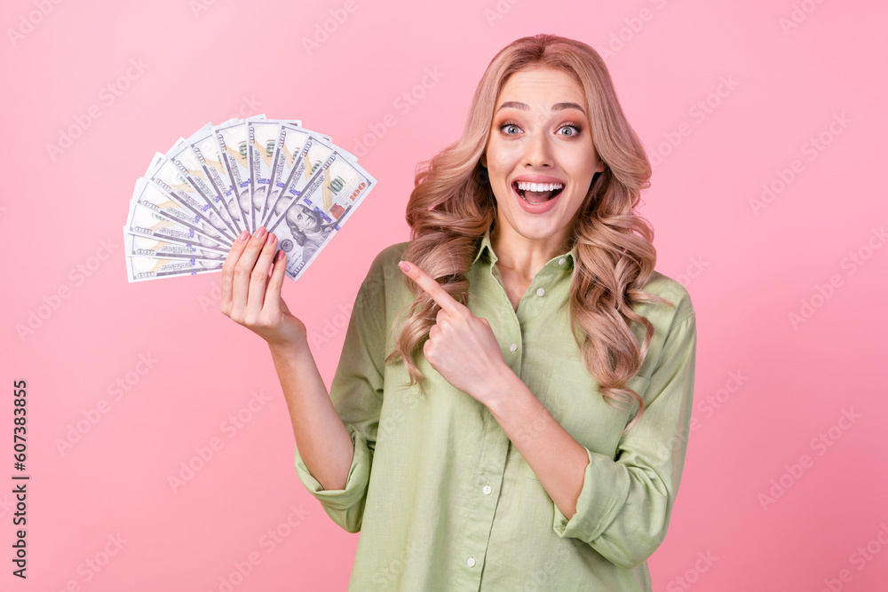 Photo of impressed positive girl indicate finger arm hold dollar bills banknotes isolated on pink color background Photo of impressed positive girl indicate finger arm hold dollar bills banknotes isolated on pink color background