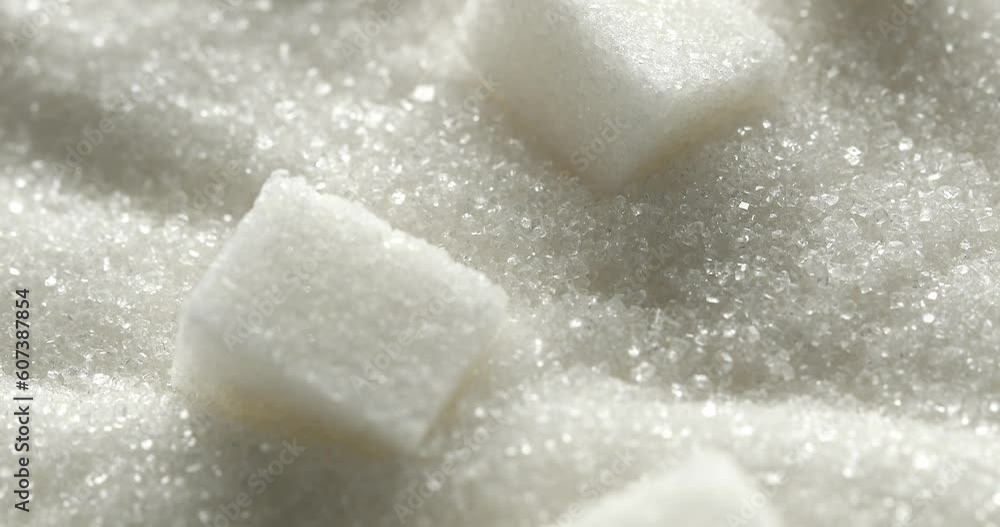 Refined Sugar Cubes on the Surface of White Sugar macro. Close up. Slow motion. Hard pieces of sugar crumble in a pile of granulated sugar. Granules. Texture, abstract background. Particles. Diabetes.