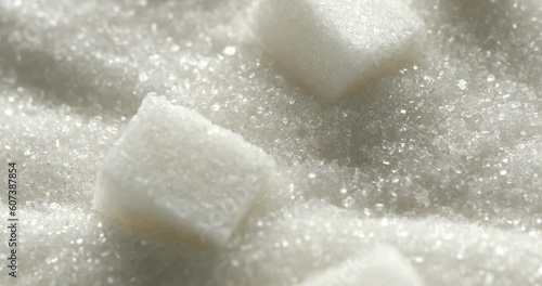 Refined Sugar Cubes on the Surface of White Sugar macro. Close up. Slow motion. Hard pieces of sugar crumble in a pile of granulated sugar. Granules. Texture, abstract background. Particles. Diabetes.