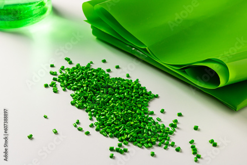 Green plastic granules near the polymer film. Raw material for the production of plastic products.