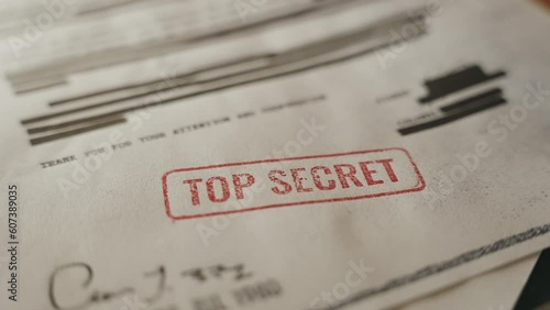Government of agency official paper with Top Secret red stamp is set on the desk. Paper with sensitive information and data is set down by hand on pile of leaked or exposed classified files and docs photo