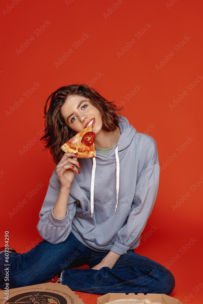 a young girl on an orange background in casual clothes bites a pizza a young girl on an orange background in casual clothes bites a pizza