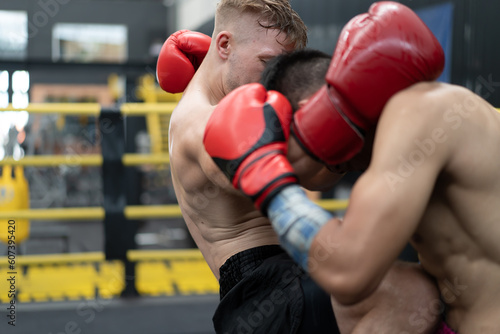 Two male athlete boxing competition in ring. Diverse ethnic men punch fighting in kickboxing exercise in fitness gym. Boxing is fighter sport training need body strength and power fist to knockout. © Nassorn