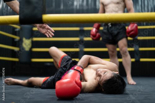 Unconscious Asian boxer lay on floor referee counting down knockout in the ring at fitness gym. Boxing is fighter sport training need body muscular strength, power fist and sweating to become champion photo