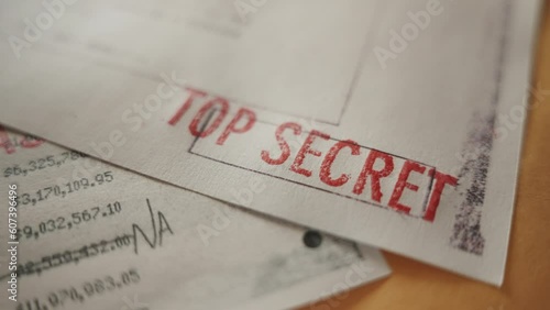 Classified official looking paper with Top Secret red stamp is laid on desk. Close up on the red stamp marked for security clearance level by government agency or exposed declassified or leaked files photo