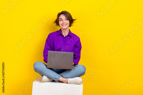 Full length portrait of charming positive person sit podium hold netbook look empty space isolated on yellow color background