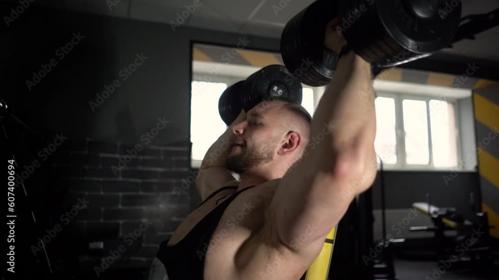 A strong male bodybuilder shakes his biceps in the gym with a barbell and dumbbells, at this time the muscles are tense A strong male bodybuilder shakes his biceps in the gym with a barbell and dumbbells, at this time the muscles are tense
