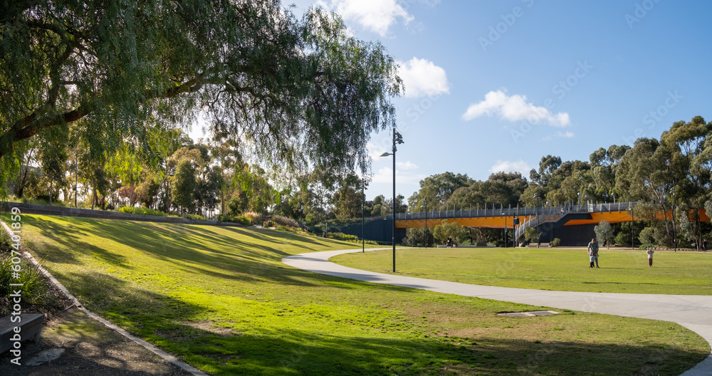 A public urban park with a large open outdoor space, well-maintained grass lawn, and a footbridge in the background. Unidentified man and children playing together in the distance. Copy space A public urban park with a large open outdoor space, well-maintained grass lawn, and a footbridge in the background. Unidentified man and children playing together in the distance. Copy space