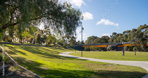 Fototapeta Naklejka Na Ścianę i Meble -  A public urban park with a large open outdoor space, well-maintained grass lawn, and a footbridge in the background. Unidentified man and children playing together in the distance. Copy space