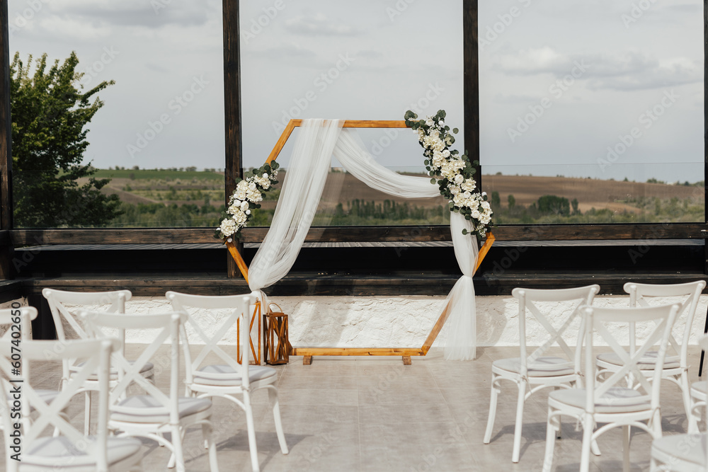 Wedding wooden arch in rustic style decorated with white flowers and greenery. Wooden hexagonal arch and flower decoration. Wedding ceremony in sunny summer day.