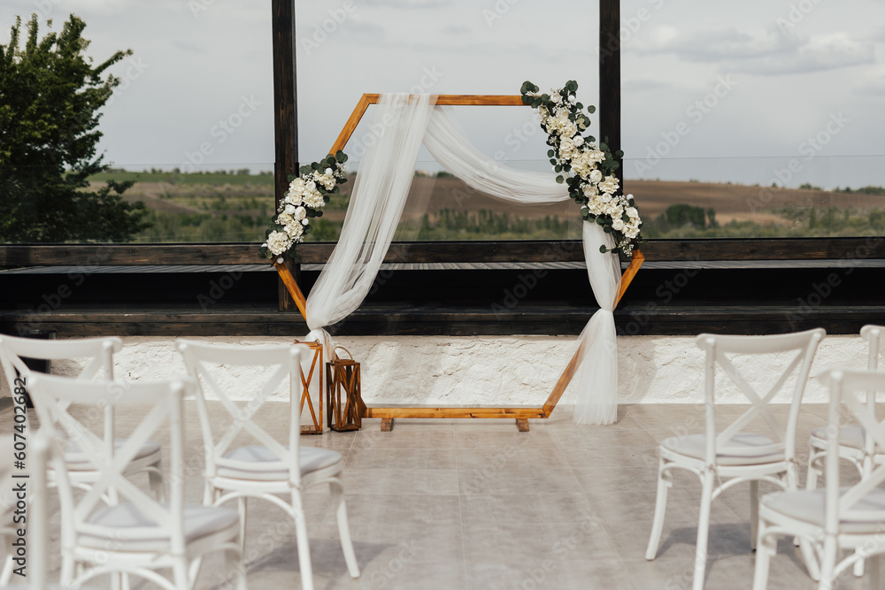 Wedding wooden arch in rustic style decorated with white flowers and greenery. Wooden hexagonal arch and flower decoration. Wedding ceremony in sunny summer day.