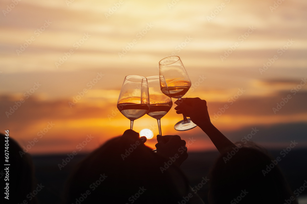 A group of girlfriends raise a toast with glasses of white wine on a sunset. Close shot.