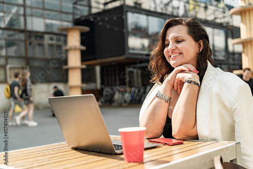 Freelance Female influencer blogger, comfortable working outdoors in a cafe using a laptop and drinking coffee.