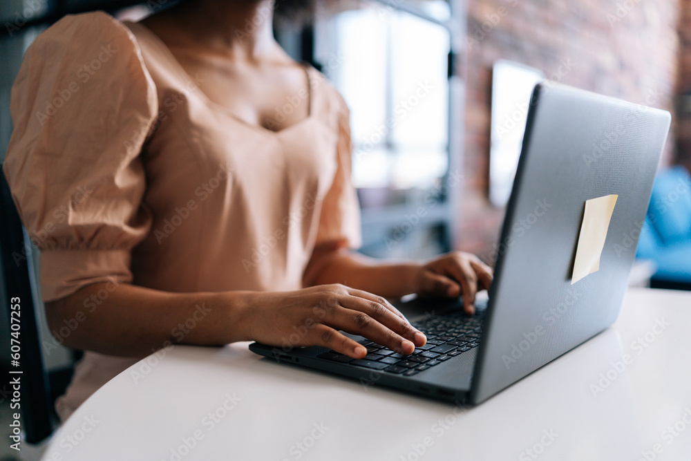 Fototapeta premium Close-up hands of unrecognizable African female student typing on notebook keyboard studying working online. Closeup of black businesswoman typing on laptop computer at desk from remote home office.