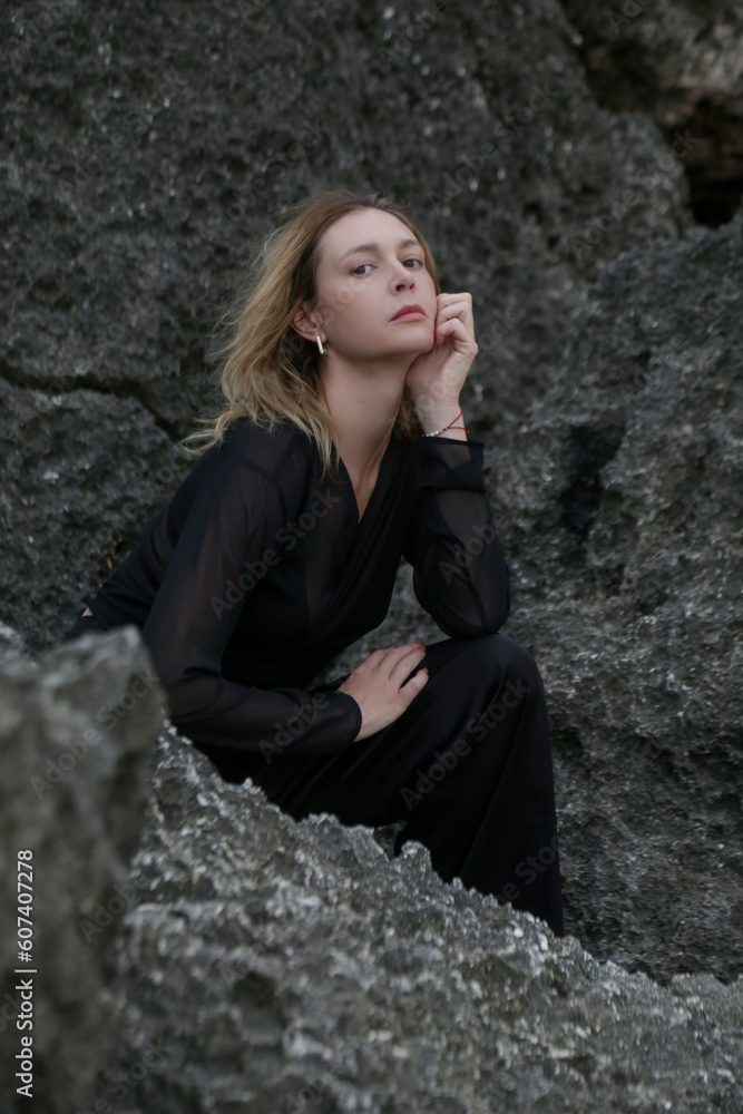 Stylish fashionable model in black outfit posing on rocks sea coast Stylish fashionable model in black outfit posing on rocks sea coast