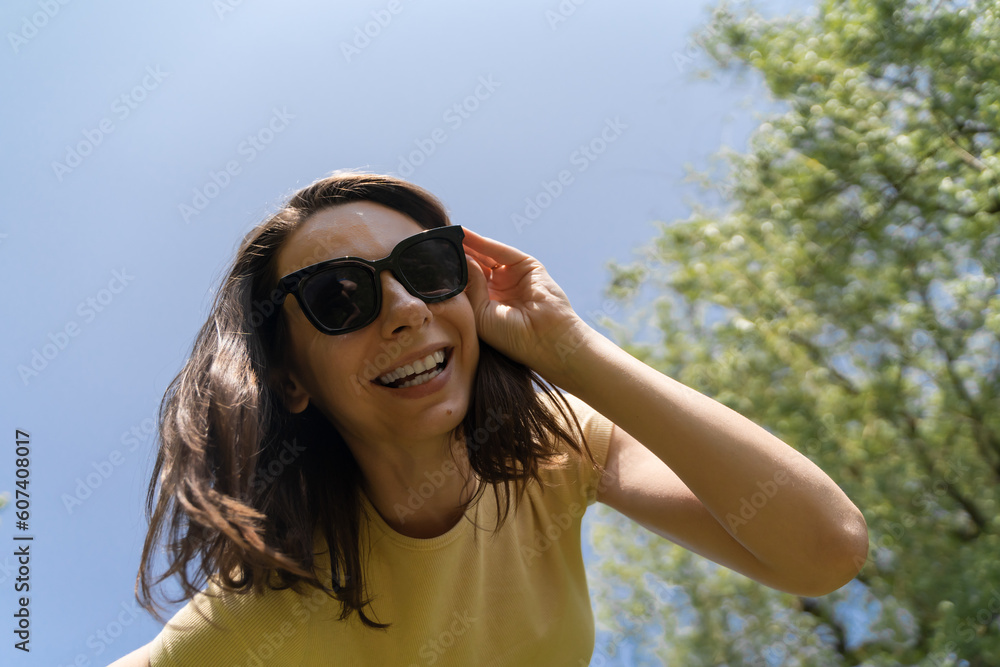 Bottom view of happy millennial woman in yellow t-shirt and sunglasses smiling broadly, looking directly to the camera. Bottom view of happy millennial woman in yellow t-shirt and sunglasses smiling broadly, looking directly to the camera.
