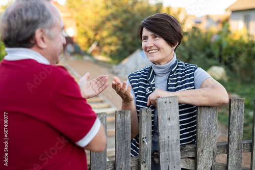 Neighbors standing at fence outdoors and having conversation. Village residents talking photo