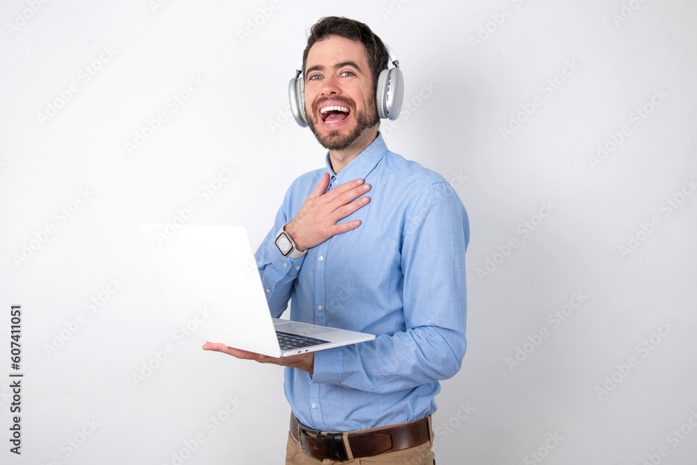 businessman wearing blue t-shirt with headphones over white background smiles toothily cannot believe eyes expresses good emotions and surprisement businessman wearing blue t-shirt with headphones over white background smiles toothily cannot believe eyes expresses good emotions and surprisement